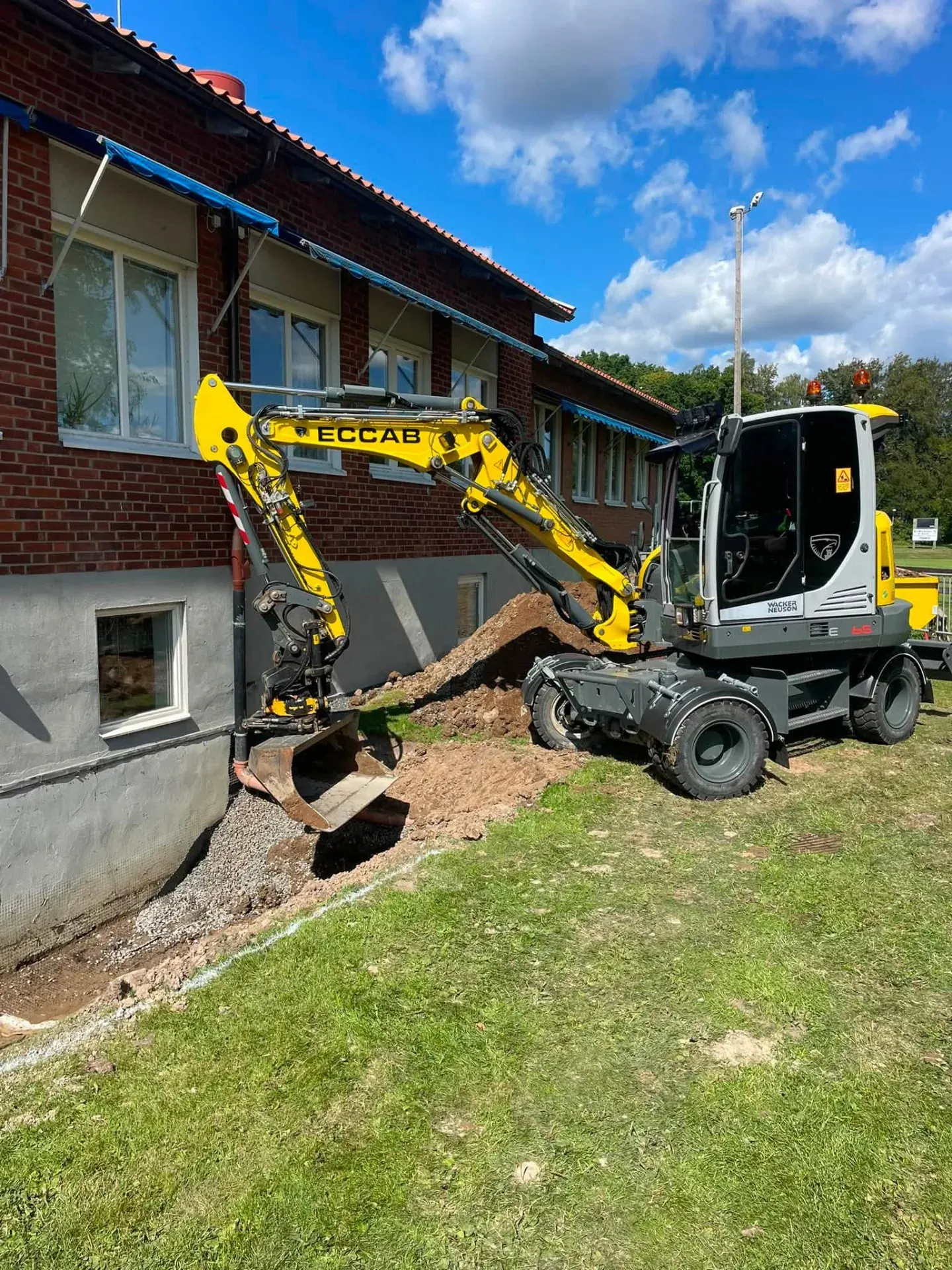 ECCAB:s gula grävmaskin utför dräneringsarbete intill en husgrund